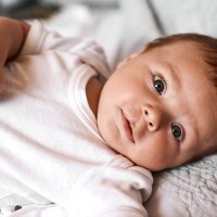 Baby, portrait and kid on bed with relax for wellness, child development or comfortable in bedroom. Young, newborn and infant boy in nursery for curiosity, growth or morning routine in home.