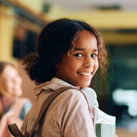 Happy African American high school student walking through hallway with her friends and looking at camera.